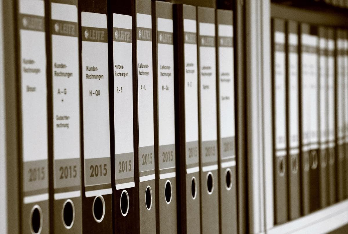 Una fila de archivadores de palanca etiquetados que archivan documentos en una estantería — el almacenamiento de conocimiento cero mantiene tus documentos sellados para que solo tú puedas abrirlos.